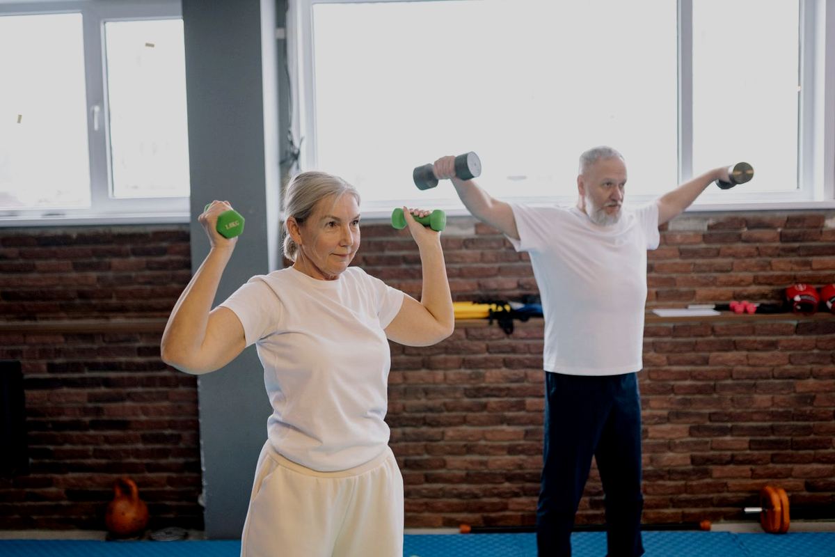 An older couple training together with dumbbells, looking engaged and active