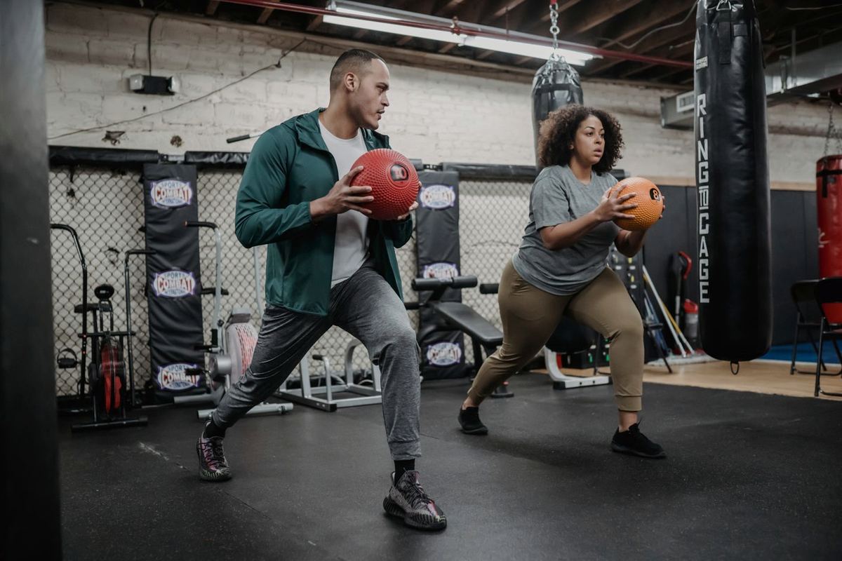 A new gym-goer learning a medicine-ball squat alongside a more experienced training partner