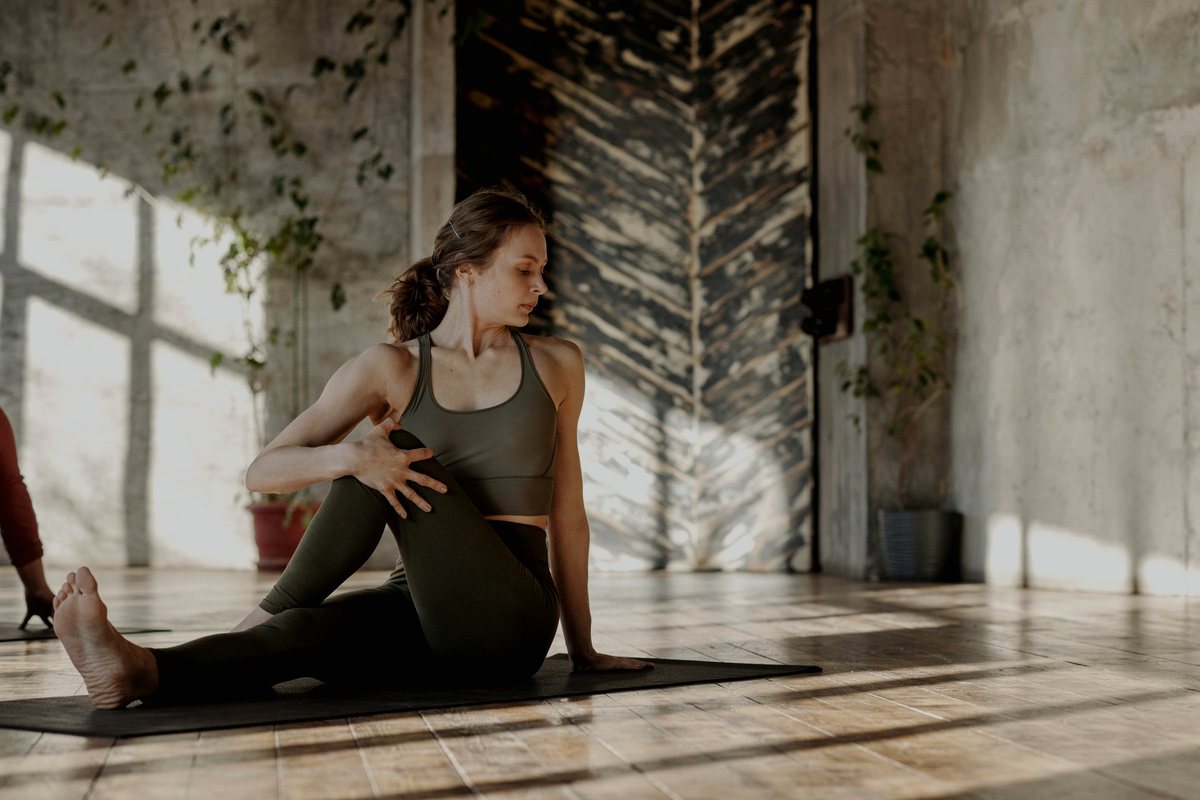 Person seated on a gym mat in olive athletic wear, twisting through an active mobility stretch
