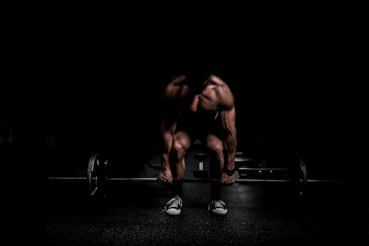 An athlete in a dark gym lifting a loaded barbell off the floor with visible effort